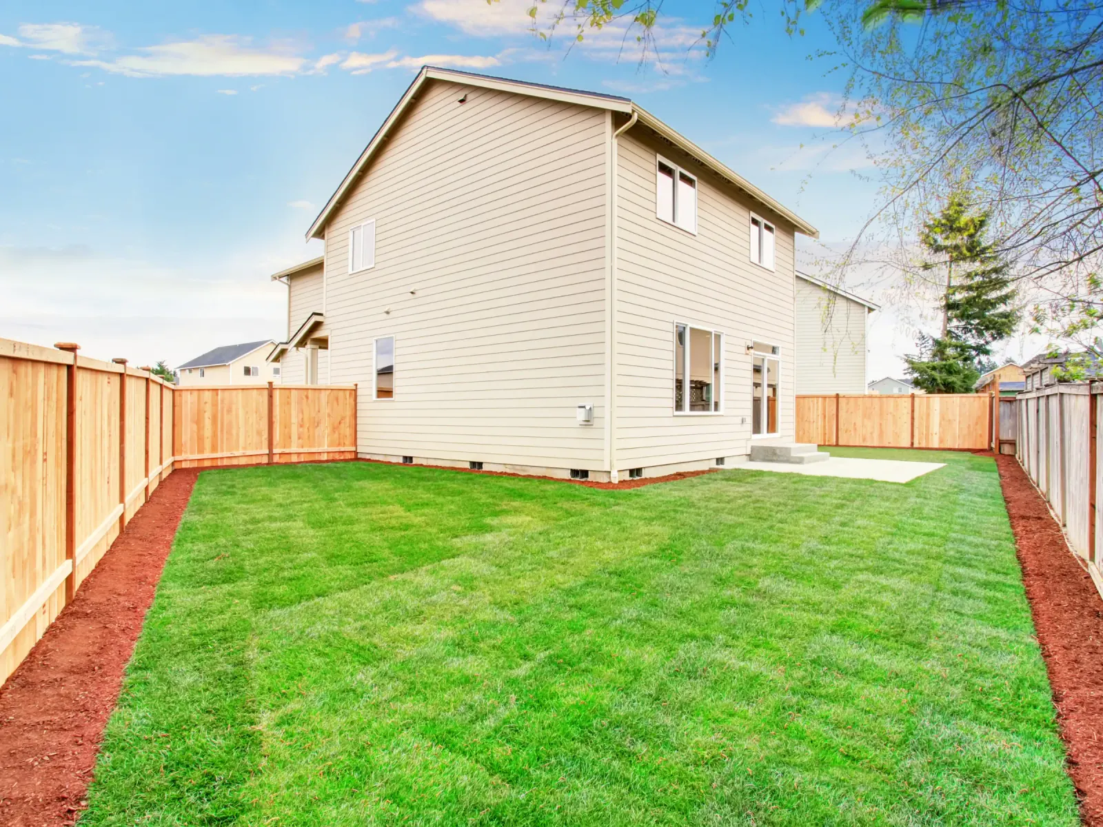 A new home's fenced back yard with fresh green sod and mulched borders